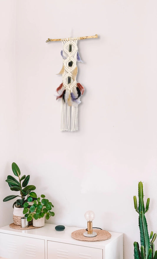 Tenture macramé Cherokee accrochée au mur au-dessus d'un meuble blanc avec des plantes